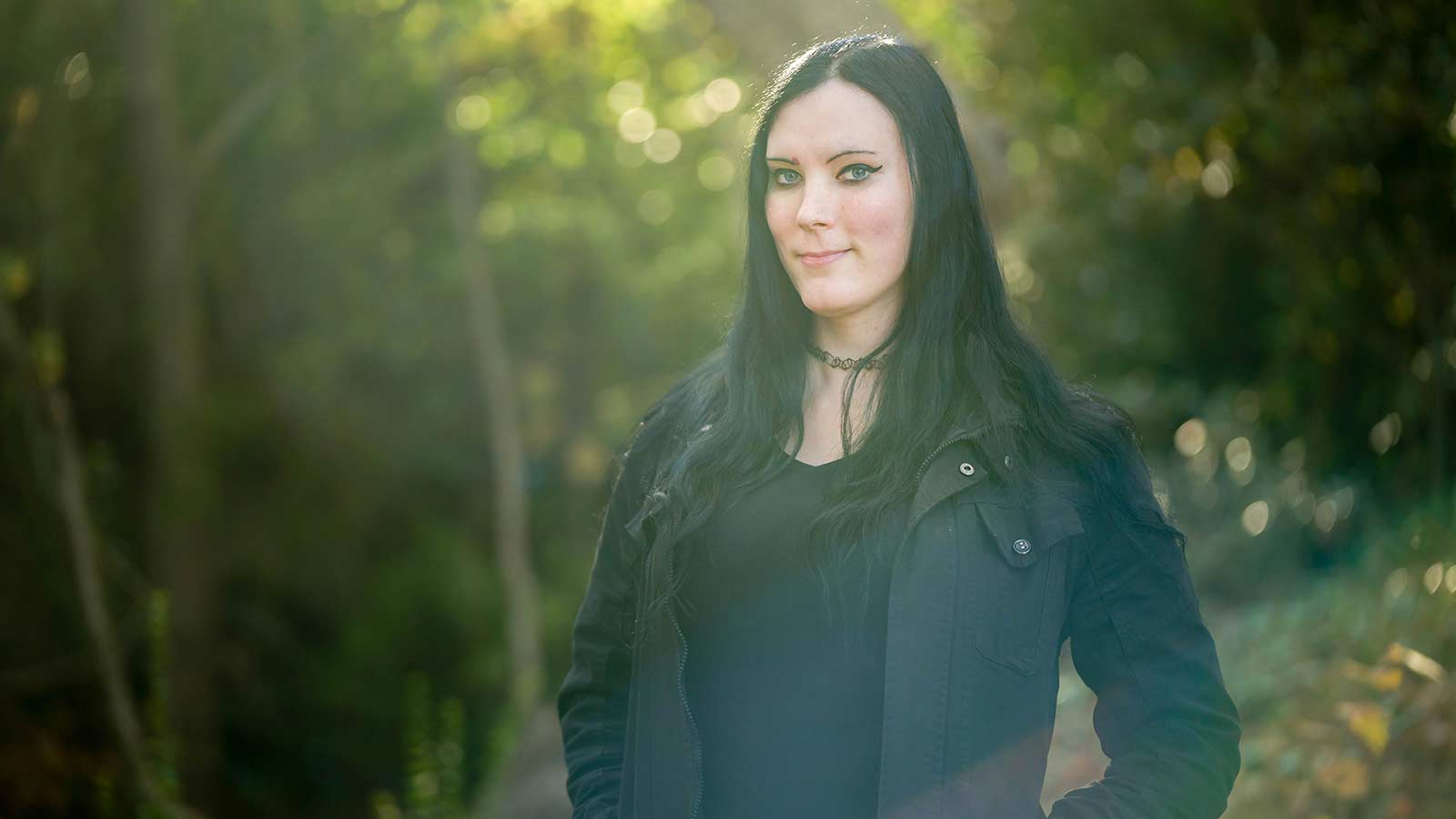 Tessa who has long, black hair wearing a black shirt and jacket, and backlit by the afternoon sun.